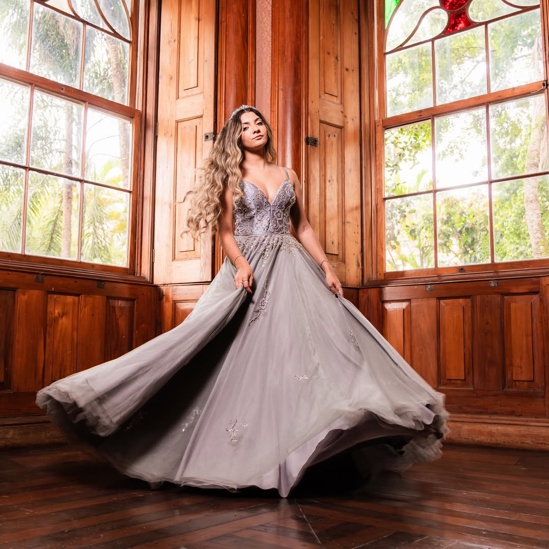 Debutante em vestido prateado rodopiando em salão de madeira com vitrais coloridos